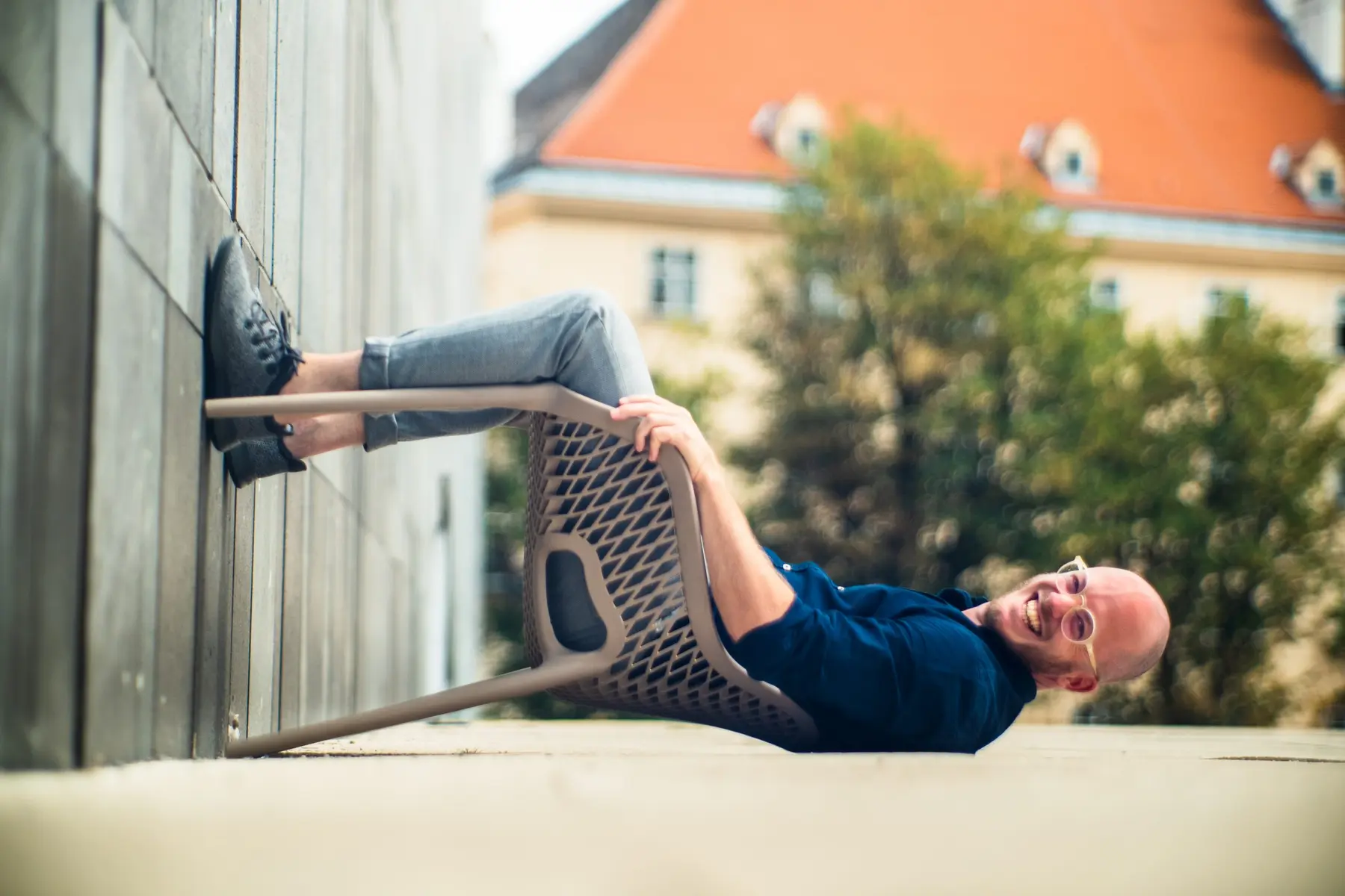 Bernhard Reingruber liegt lachend mit einem gekippten Sessel an einer Wand.